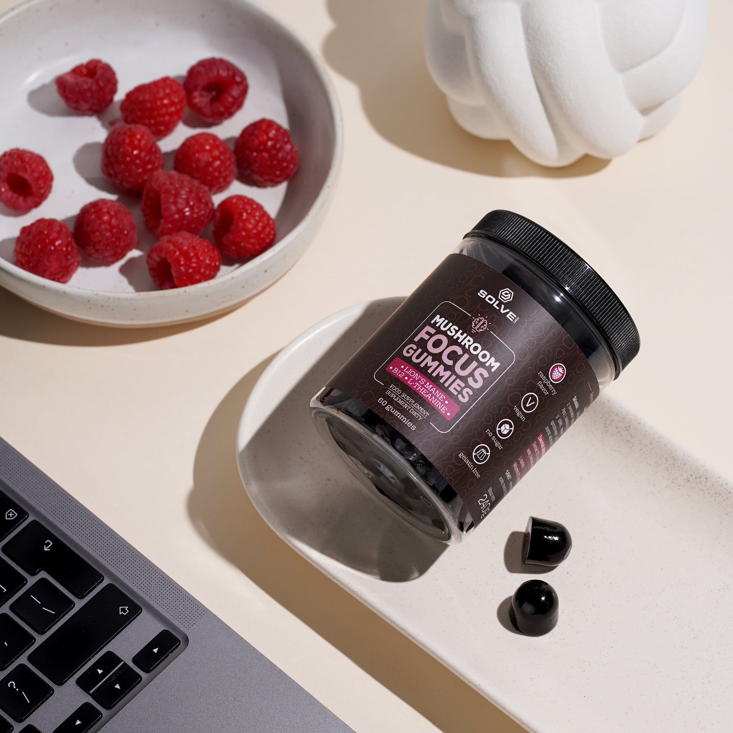 Supplement container labeled 'Nootropic Focus Gummies' on a light surface with raspberries and a laptop.